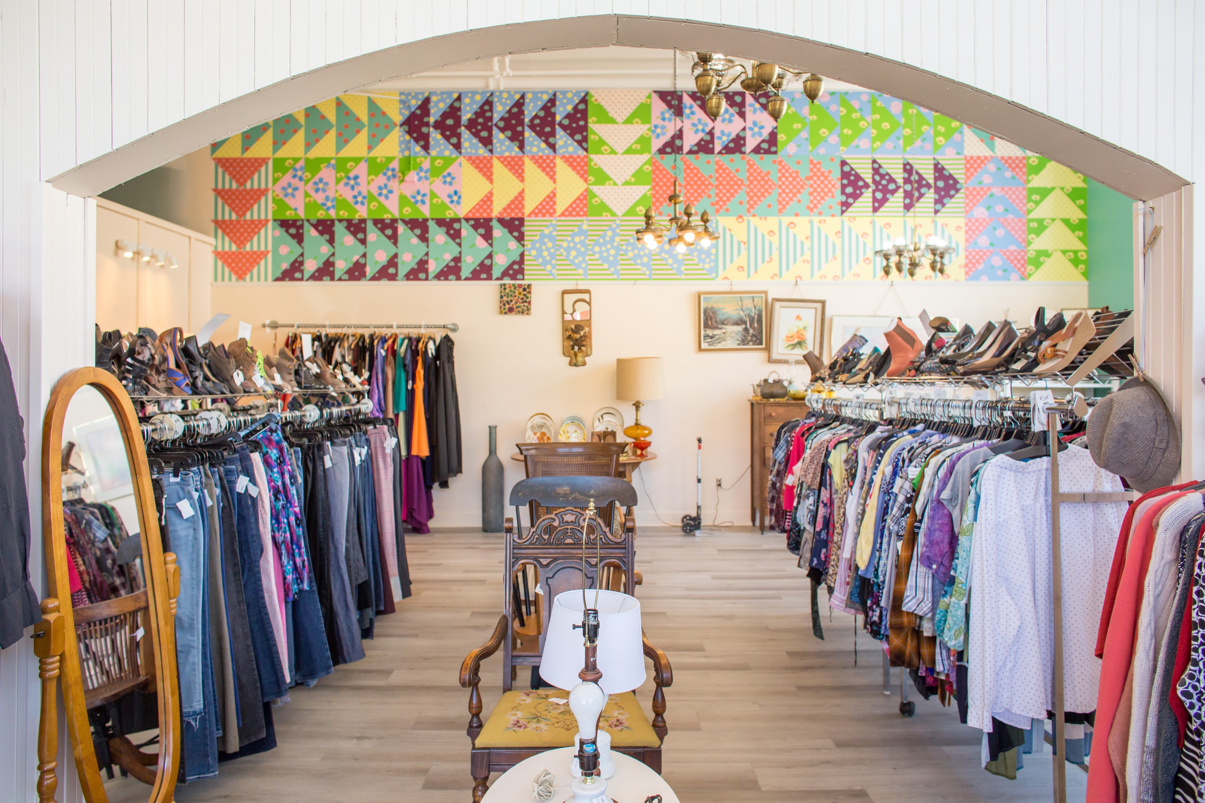 A resale boutique interior with clothing racks on both sides, a patterned quilt mural painted above.